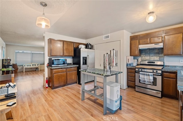 kitchen featuring backsplash, a textured ceiling, decorative light fixtures, light hardwood / wood-style floors, and stainless steel appliances