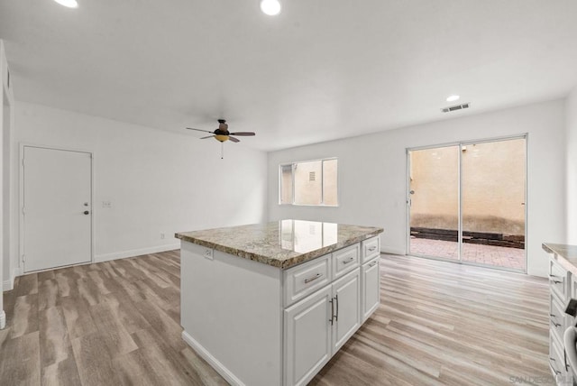 kitchen with a center island, white cabinets, light stone counters, and light hardwood / wood-style flooring