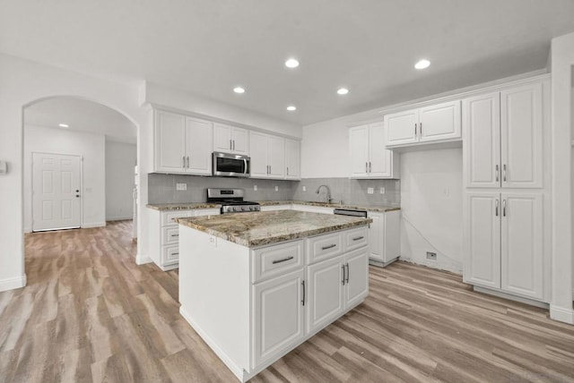 kitchen featuring sink, stainless steel appliances, a center island, light stone countertops, and white cabinets