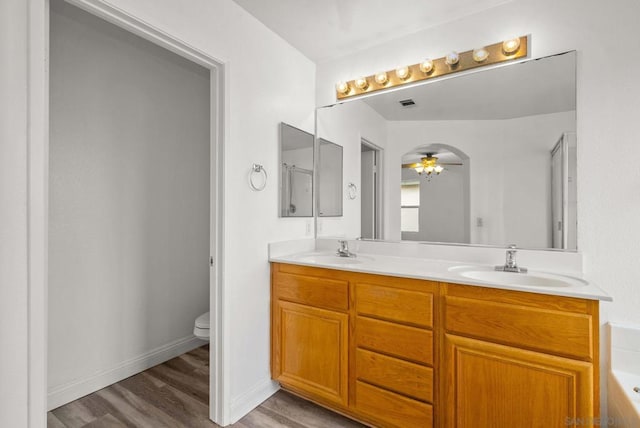 bathroom with toilet, vanity, ceiling fan, hardwood / wood-style floors, and a washtub