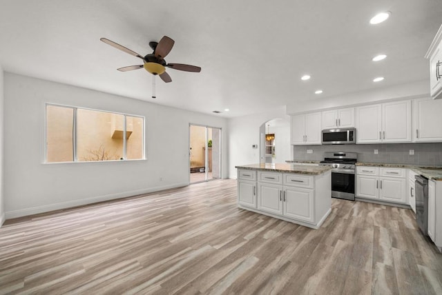 kitchen with stainless steel appliances, a center island, light stone counters, white cabinets, and light wood-type flooring