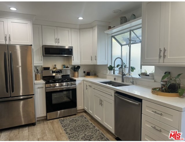 kitchen featuring appliances with stainless steel finishes, white cabinetry, sink, light stone counters, and light wood-type flooring