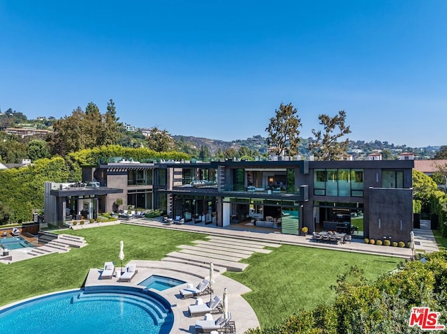 rear view of house featuring a swimming pool with hot tub, a patio, and a lawn