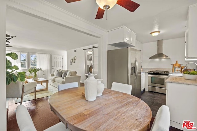 dining area with dark wood-type flooring, sink, crown molding, ceiling fan, and a barn door