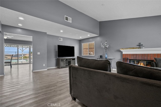 living room with lofted ceiling, light hardwood / wood-style flooring, a textured ceiling, ceiling fan, and a fireplace