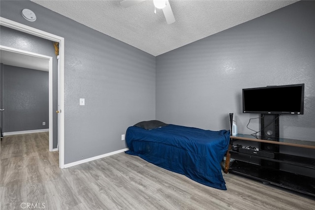 bedroom with ceiling fan, vaulted ceiling, a textured ceiling, and light wood-type flooring