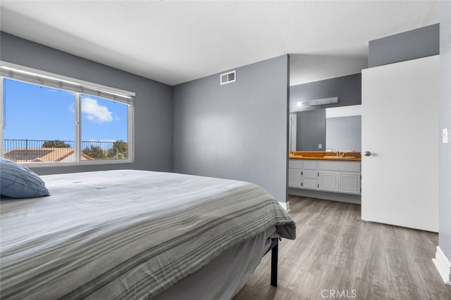 bedroom featuring connected bathroom, sink, a textured ceiling, and light wood-type flooring