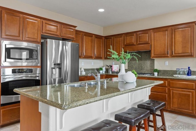 kitchen featuring a kitchen island with sink, sink, appliances with stainless steel finishes, and a kitchen bar