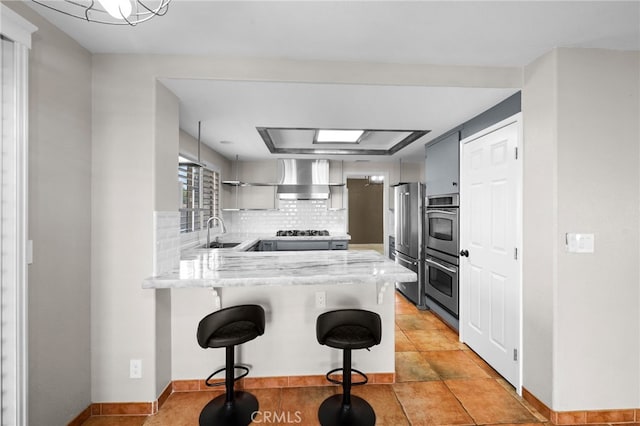 kitchen featuring wall chimney exhaust hood, a kitchen bar, kitchen peninsula, stainless steel appliances, and backsplash