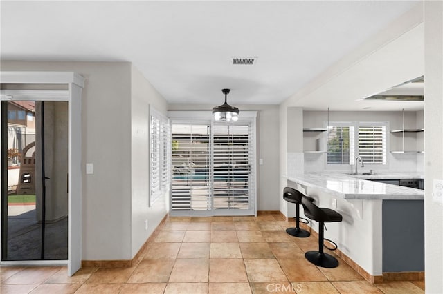 interior space with sink, light tile patterned floors, a breakfast bar area, tasteful backsplash, and decorative light fixtures