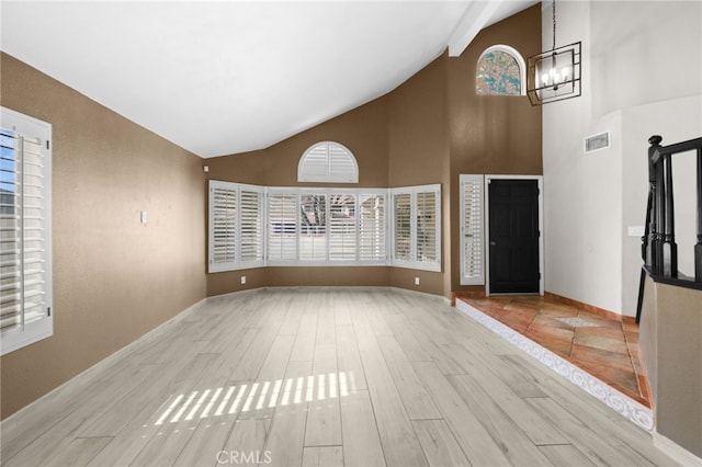 unfurnished living room featuring high vaulted ceiling, a notable chandelier, and light wood-type flooring