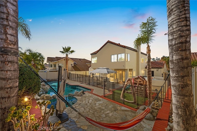 playground at dusk featuring a fenced in pool and a patio