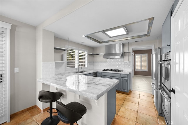 kitchen featuring sink, gray cabinets, a kitchen breakfast bar, kitchen peninsula, and wall chimney exhaust hood