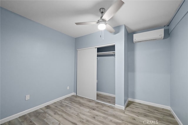 unfurnished bedroom with ceiling fan, a wall mounted AC, light hardwood / wood-style floors, and a closet