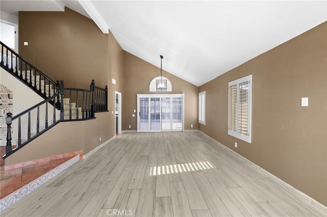 unfurnished living room with an inviting chandelier, high vaulted ceiling, and light hardwood / wood-style floors