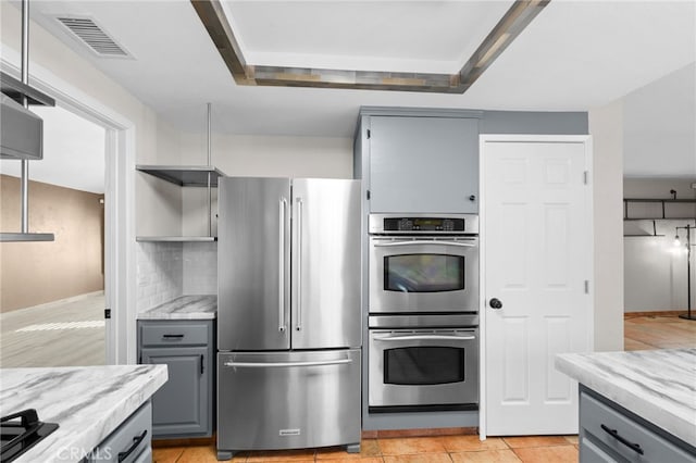 kitchen featuring light tile patterned floors, a tray ceiling, gray cabinets, stainless steel appliances, and backsplash