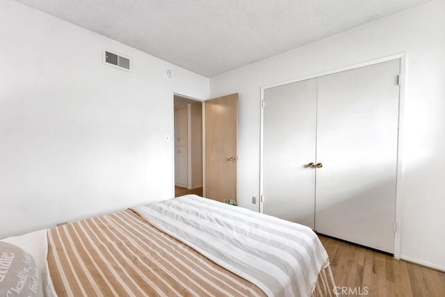 bedroom with a closet, a textured ceiling, and light hardwood / wood-style flooring