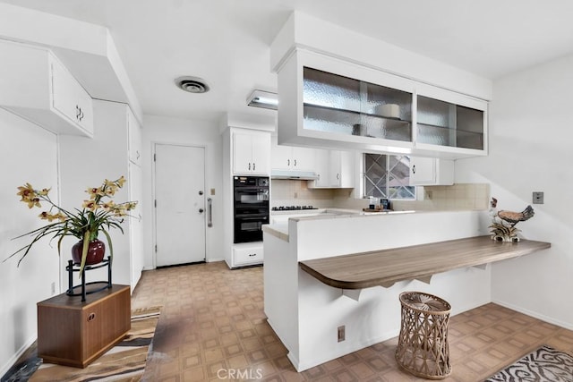 kitchen with a kitchen bar, black appliances, kitchen peninsula, white cabinets, and backsplash