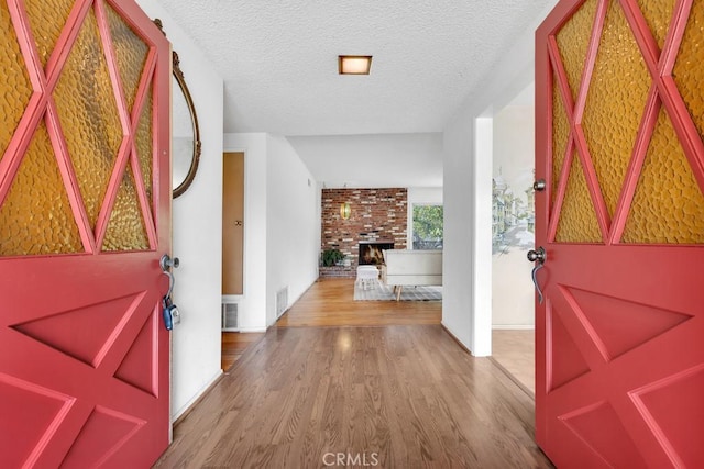 foyer entrance with a brick fireplace, hardwood / wood-style floors, and a textured ceiling