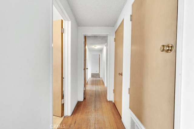 hall with a textured ceiling and light wood-type flooring