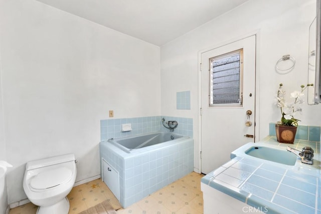 bathroom featuring vanity, tiled bath, and toilet