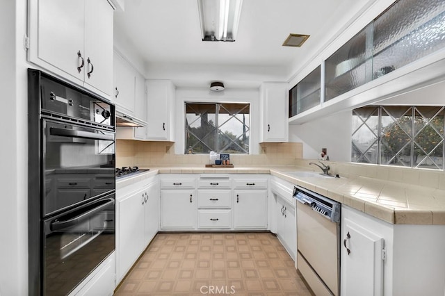 kitchen with dishwashing machine, double oven, tile counters, and white cabinets