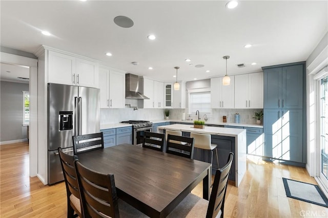 kitchen featuring wall chimney range hood, blue cabinetry, high quality appliances, white cabinets, and decorative light fixtures