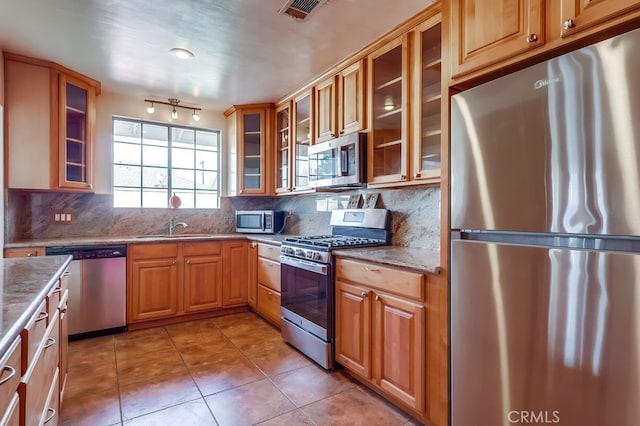 kitchen with sink, stone countertops, light tile patterned floors, appliances with stainless steel finishes, and backsplash