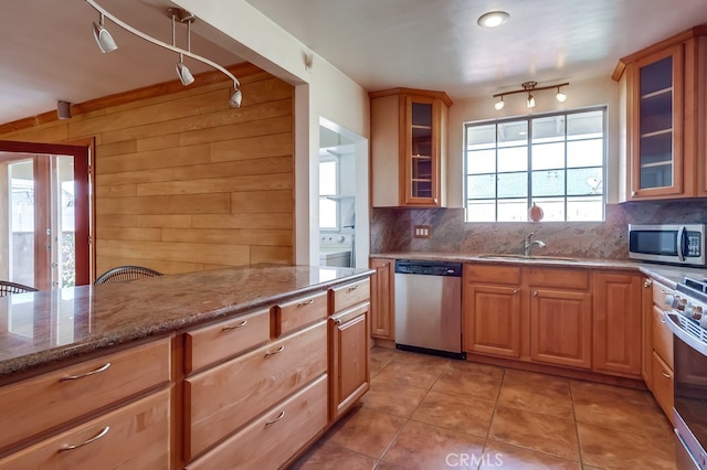 kitchen with sink, appliances with stainless steel finishes, wooden walls, light stone counters, and decorative backsplash