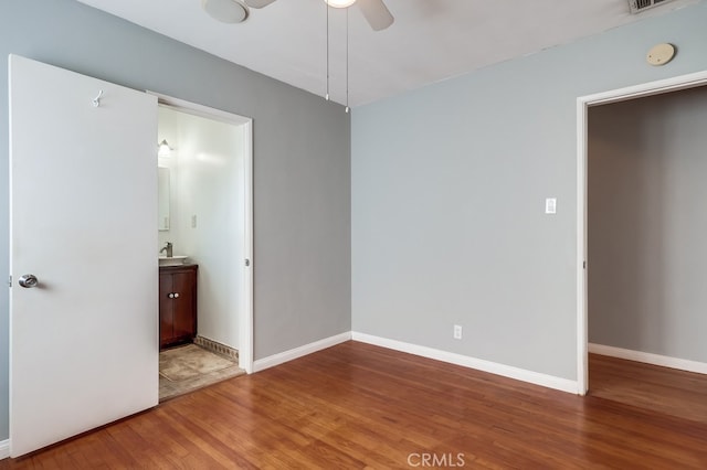 unfurnished bedroom featuring ensuite bathroom, sink, hardwood / wood-style floors, and ceiling fan