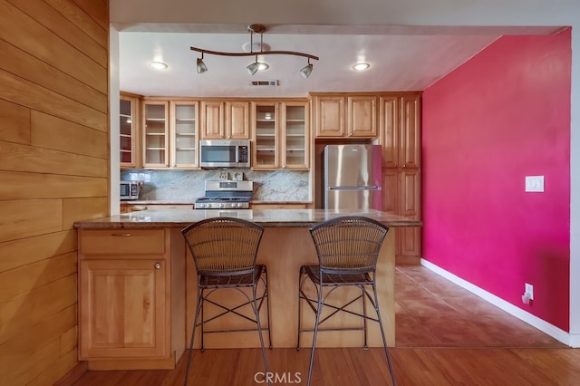 kitchen with dark stone countertops, appliances with stainless steel finishes, a kitchen breakfast bar, kitchen peninsula, and decorative backsplash