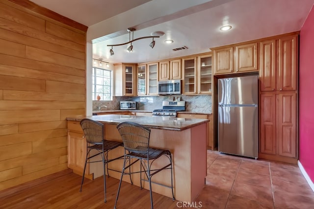 kitchen featuring a kitchen bar, wood walls, kitchen peninsula, stainless steel appliances, and backsplash