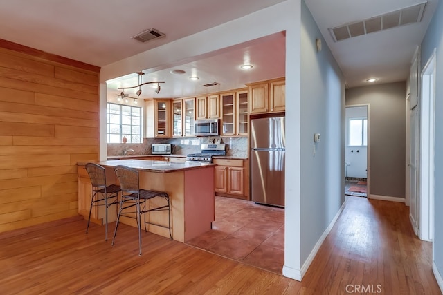 kitchen with a breakfast bar area, stainless steel appliances, tasteful backsplash, kitchen peninsula, and light wood-type flooring