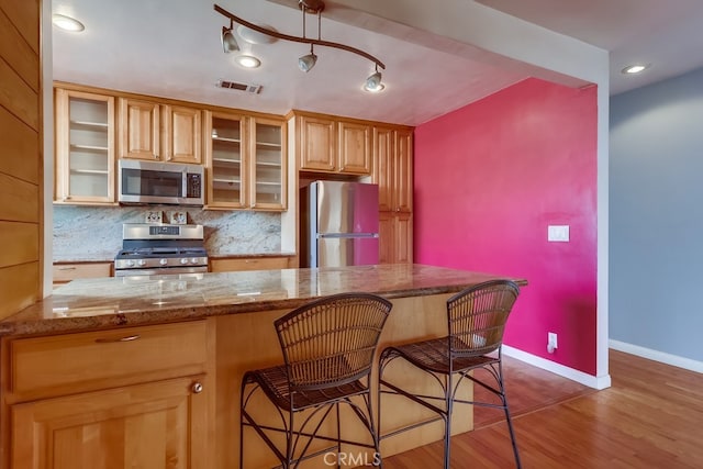 kitchen featuring hardwood / wood-style floors, a breakfast bar area, backsplash, stainless steel appliances, and light stone countertops