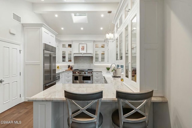 kitchen featuring a kitchen breakfast bar, high quality appliances, light stone counters, white cabinets, and kitchen peninsula