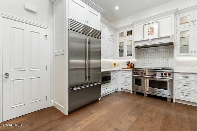 kitchen featuring dark hardwood / wood-style floors, built in appliances, tasteful backsplash, and white cabinets