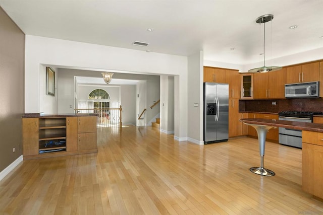 kitchen with appliances with stainless steel finishes, decorative backsplash, hanging light fixtures, kitchen peninsula, and light wood-type flooring