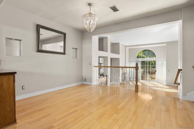 unfurnished room with a notable chandelier and light wood-type flooring