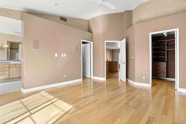 unfurnished bedroom with high vaulted ceiling, connected bathroom, a walk in closet, a closet, and light wood-type flooring