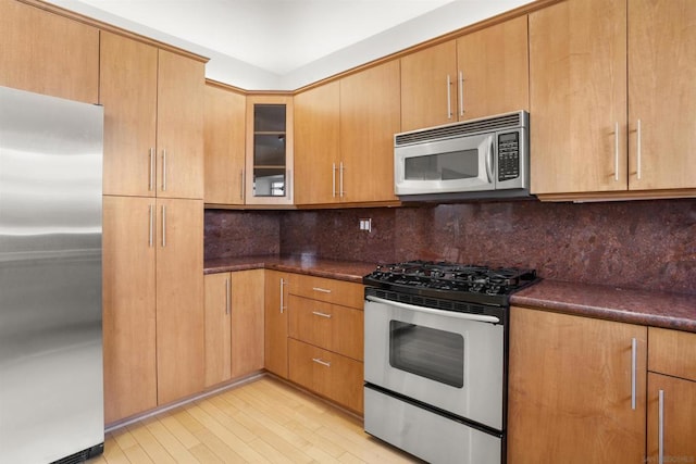 kitchen with dark stone countertops, decorative backsplash, light wood-type flooring, and appliances with stainless steel finishes