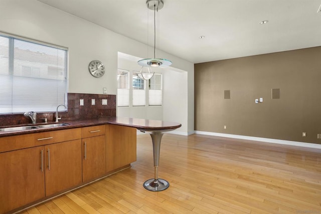 kitchen with a kitchen bar, sink, pendant lighting, light hardwood / wood-style floors, and decorative backsplash