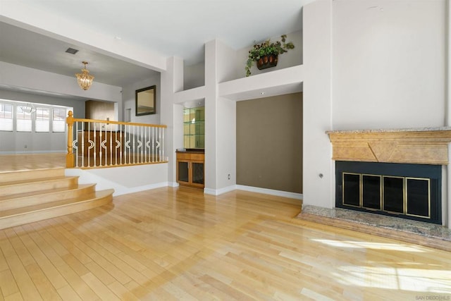 unfurnished living room with hardwood / wood-style flooring, an inviting chandelier, and a high end fireplace