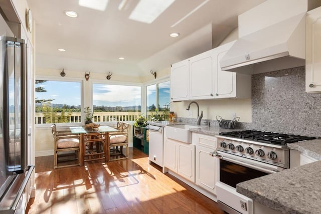 kitchen featuring sink, stainless steel range, light stone countertops, white cabinets, and wall chimney exhaust hood