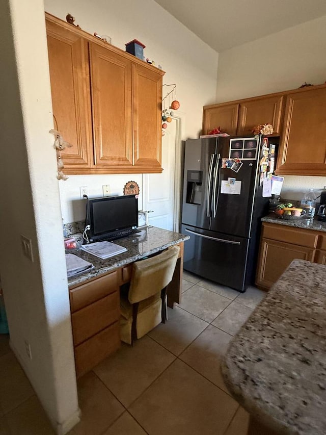 kitchen featuring stainless steel refrigerator with ice dispenser, built in desk, dark stone counters, and light tile patterned floors