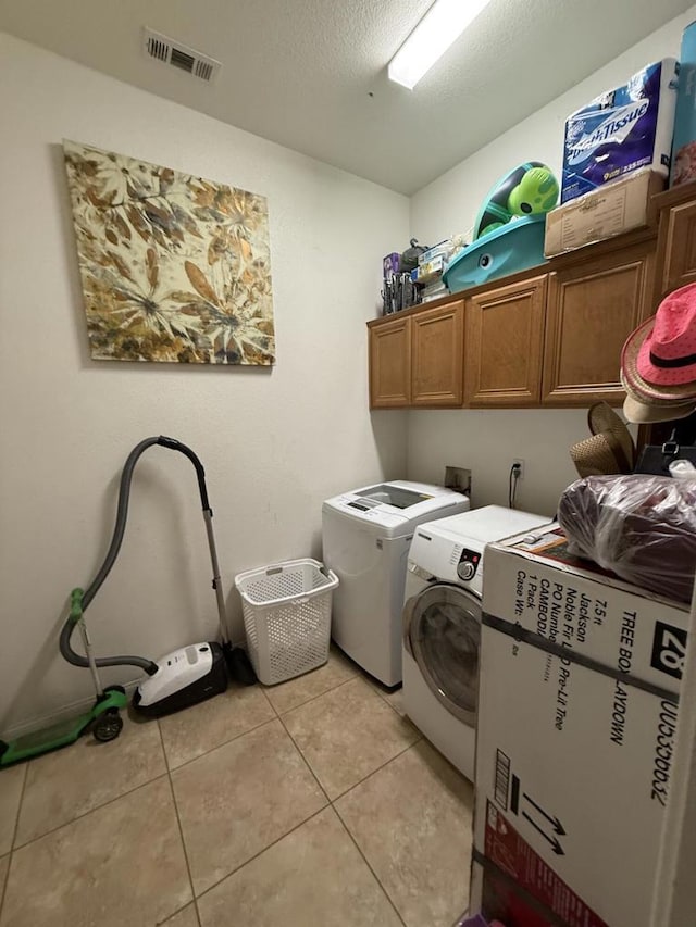 laundry room with cabinets, light tile patterned floors, a textured ceiling, and washer and clothes dryer