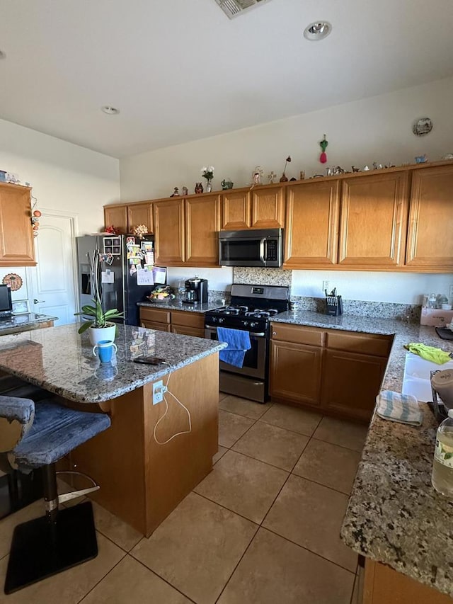 kitchen featuring light tile patterned floors, a breakfast bar area, stainless steel appliances, a center island, and light stone countertops