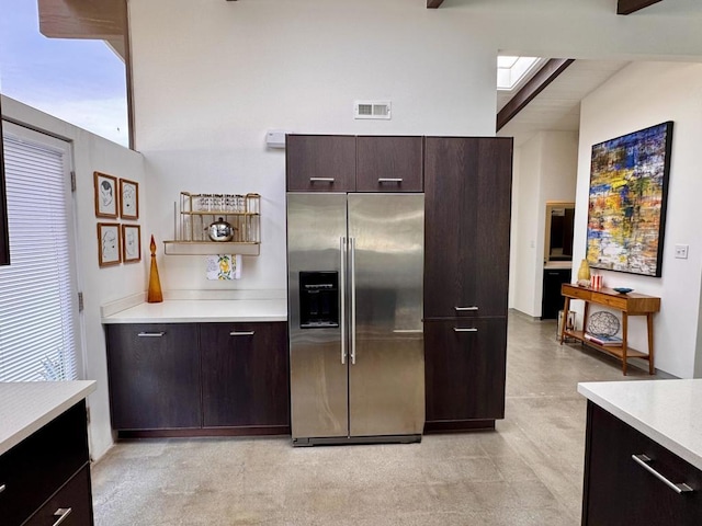 kitchen featuring a high ceiling, high end fridge, dark brown cabinetry, and a skylight