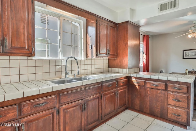 kitchen with tasteful backsplash, sink, tile counters, light tile patterned floors, and kitchen peninsula