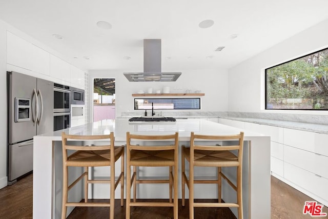 kitchen with appliances with stainless steel finishes, island range hood, a kitchen bar, and white cabinets