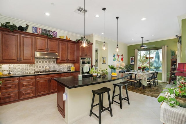 kitchen featuring pendant lighting, appliances with stainless steel finishes, a kitchen island with sink, a kitchen breakfast bar, and tasteful backsplash